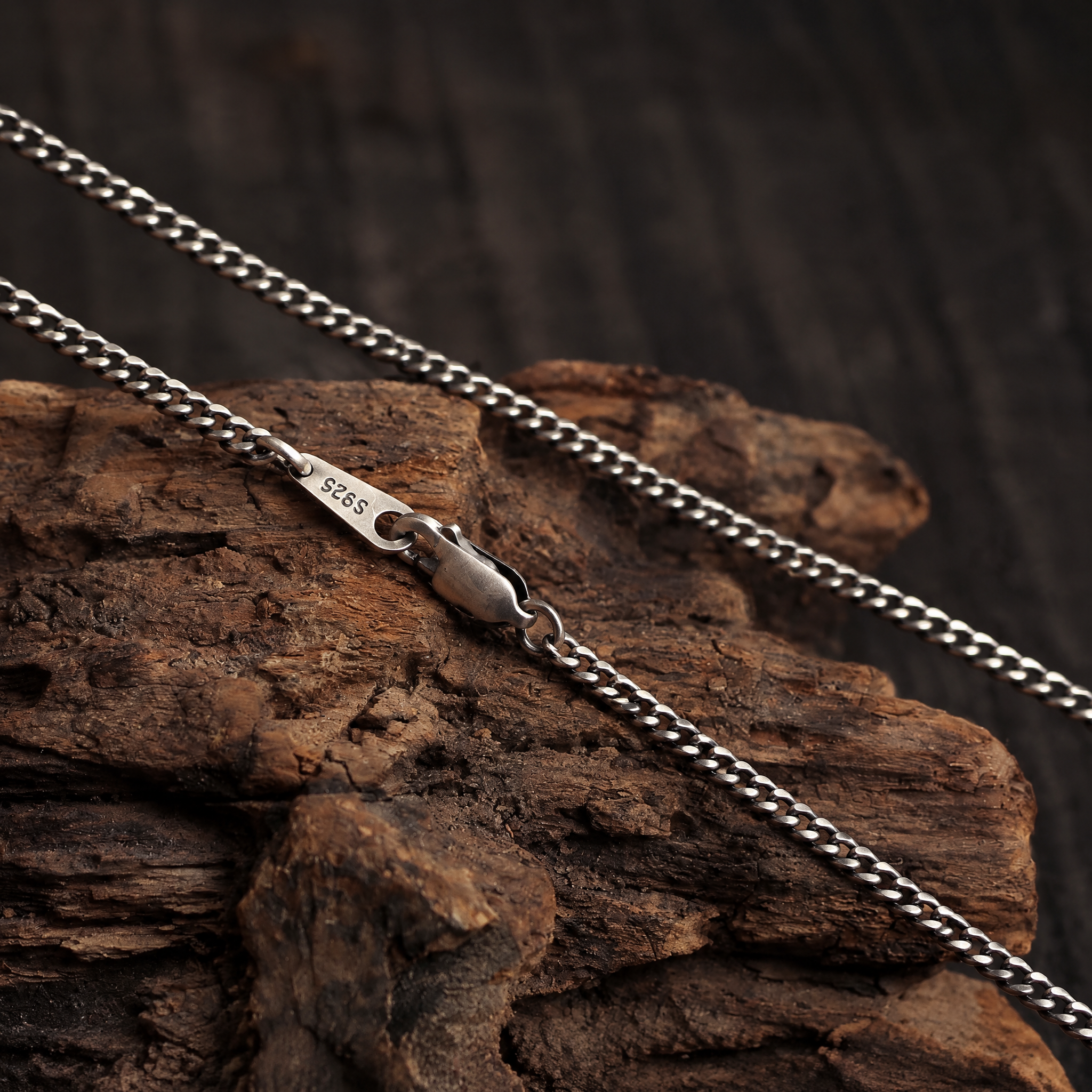 Cuban link chain with a closed lobster clasp and S925 tag stretched across rustic wood.