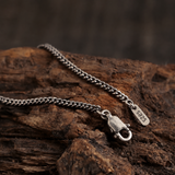 Vertical close-up of a Cuban link chain with an open lobster clasp on rustic wood.