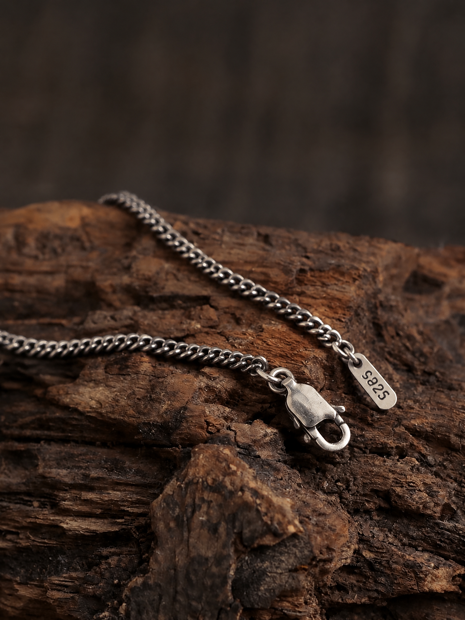 Vertical close-up of a Cuban link chain with an open lobster clasp on rustic wood.