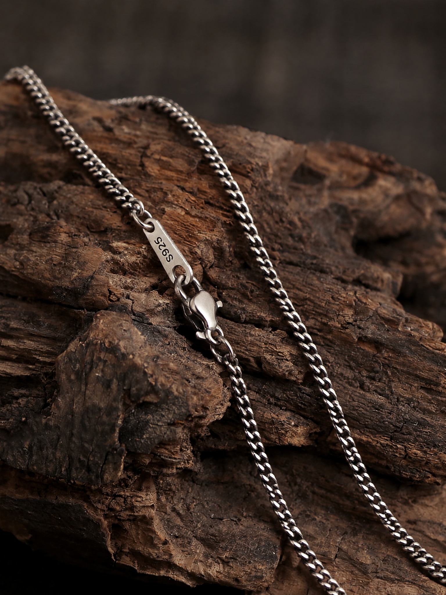 Cuban link chain draped over rustic wood, showing its links, clasp and S925 tag.