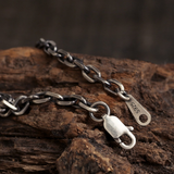 Vertical close-up of the Diamond Cut Curb Chain with an open lobster clasp beside an S925 tag on rustic wood.