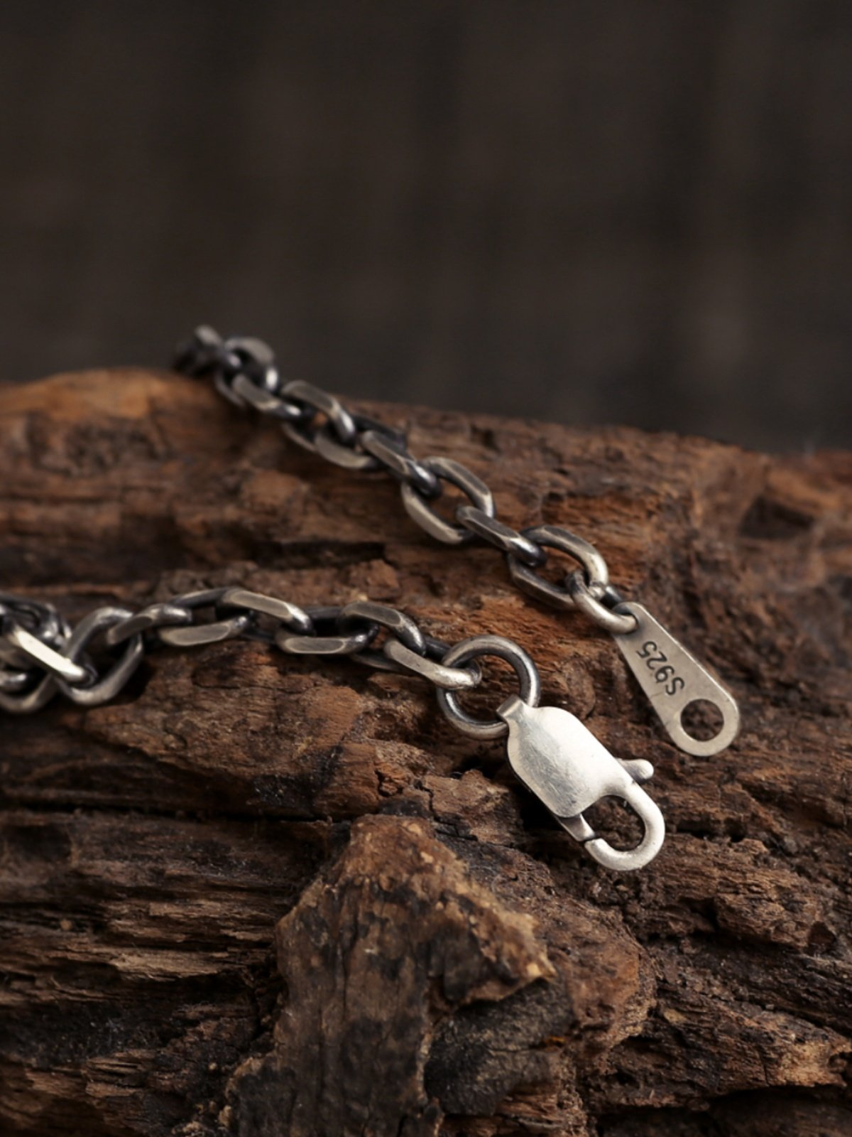 Vertical close-up of the Diamond Cut Curb Chain with an open lobster clasp beside an S925 tag on rustic wood.
